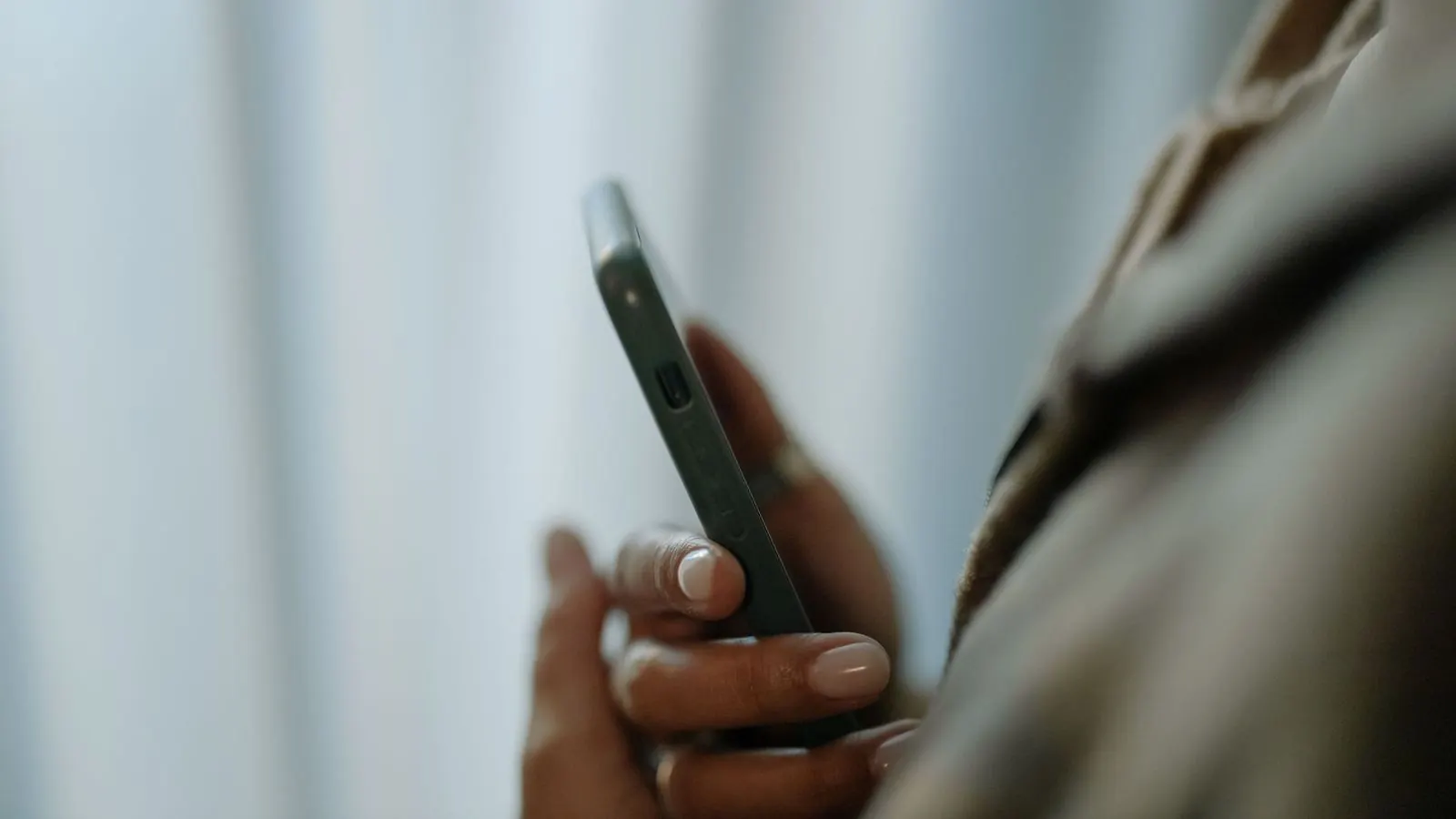 Dłoń trzymająca smartfon na tle jasnych, rozmytych zasłon