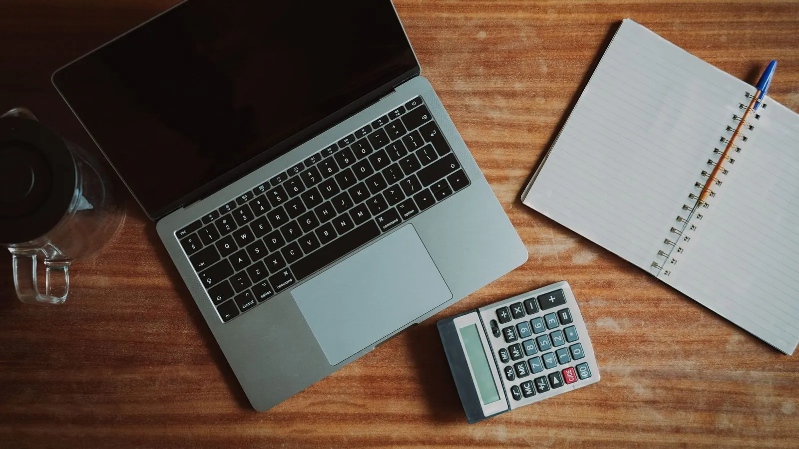 Laptop, kalkulator i otwarty notes na drewnianym biurku, widok z góry